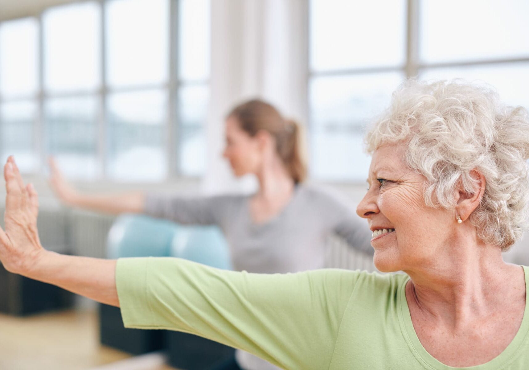 Close-up shot of elderly woman doing stretching workout at yoga class. Women practicing yoga at health club.